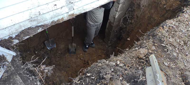 un homme se tient debout dans un trou creusé dans la terre près d’un bâtiment