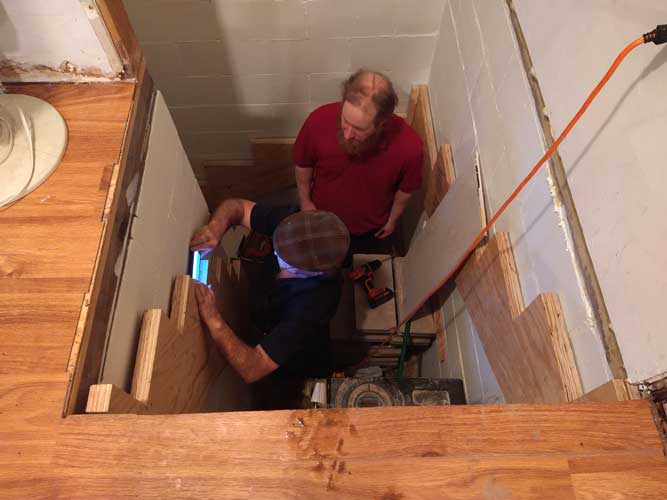 deux hommes se tiennent dans la cage d’escalier en cours de construction et vérifient que le limon est à niveau